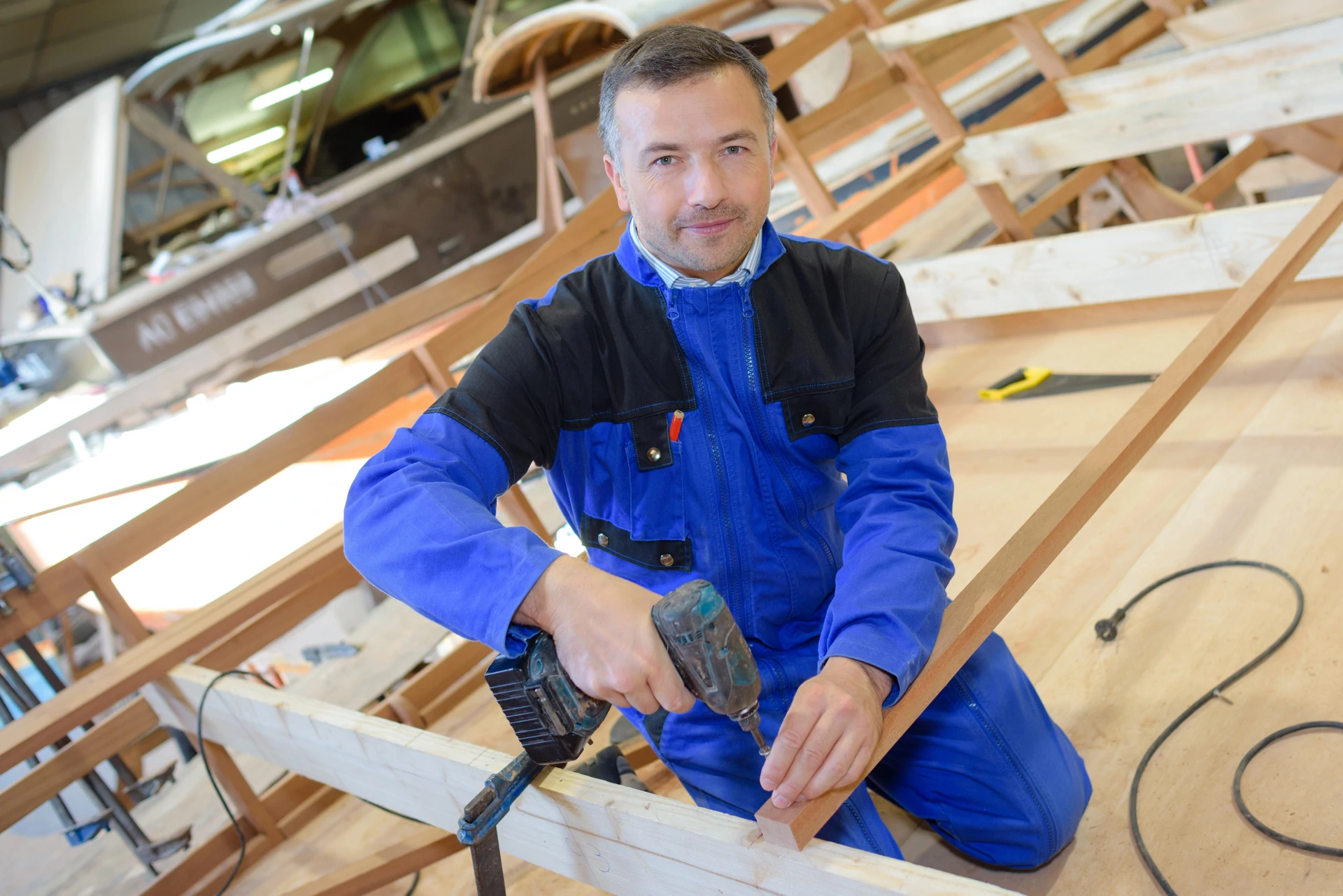 Handwerker in blauer Arbeitskleidung bohrt an einem Holzrahmen in einer Werkstatt